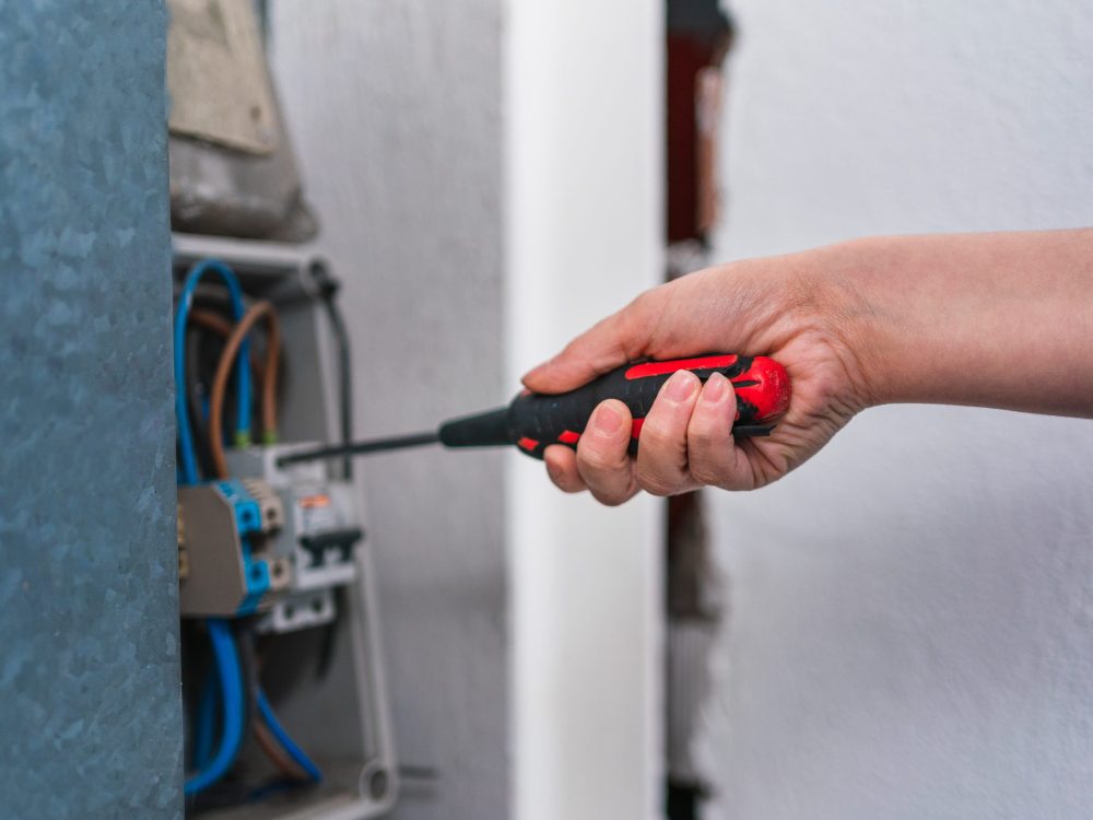 A closeup shot of hand holding a screwdriver while repairing an electrical box in the corridor