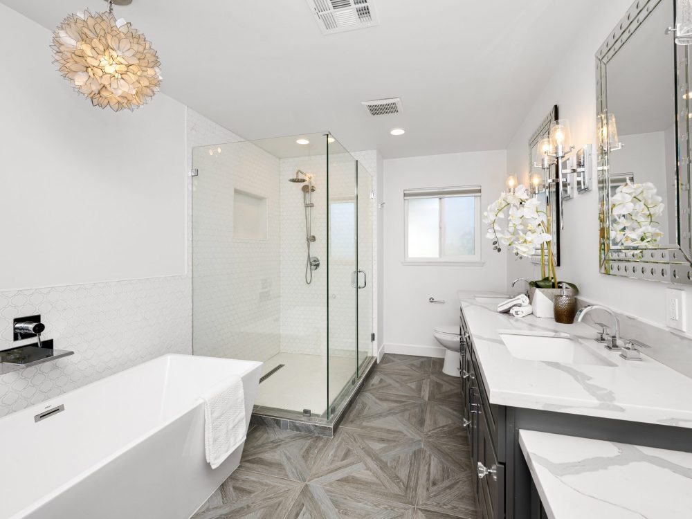 Elegant modern bathroom with wooden floors, marble counters, white tub, and two sinks